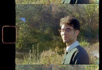 a man with glasses is standing in front of a tree